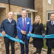 Three men and a woman cutting ribbon outside new homes